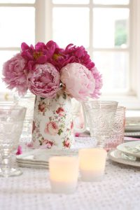 peonies fill an antique china vase behind two candles