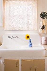 Vintage white farmhouse kitchen sink with sunflower in a vase.