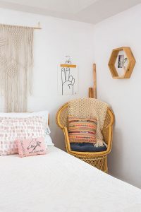 A rattan peacock chair in a white bedroom vintage cottage bedroom. A macrame textile hanging is positioned above the bed