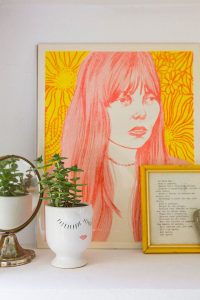A neon portrait of Joni Mitchell next to a vintage mirror and an egg-cup succulent planter