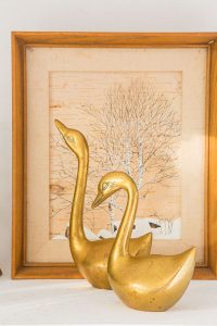 A pair of vintage brass swans in front of framed art