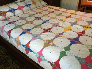 This quilt has multi-colored and patterned squares overplayed with white circles.