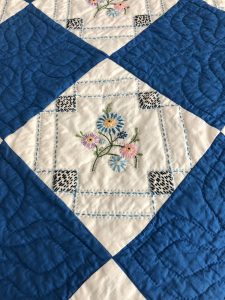 The vintage quilt is deep blue with white squares embroidered with tiny stitched flowers in each of them.