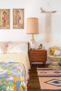 A vintage-inspired bedroom complete with a multicolor quilt, statement lamp, "Big Eye" paintings, and a slew of other antique fixtures.