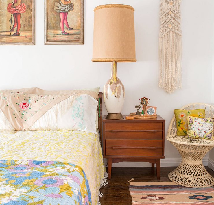 A vintage-inspired bedroom complete with a multicolor quilt, statement lamp, "Big Eye" paintings, and a slew of other antique fixtures.