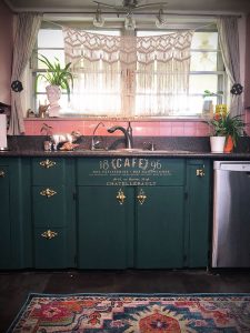 kitchen with dark green cabinets, a pink backsplash and bohemian accents.