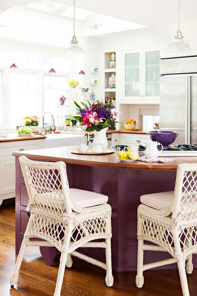 A kitchen set up with a juxtaposing purple cabinet scheme and white decor.