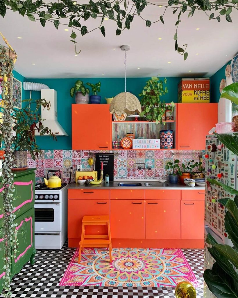 A kitchen with dark orange cabinets that complement the teal backing of the space.