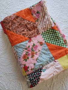 This quilt is made from multiple squares with different patterns and colors with diagonal rectangles creating "X"s across it.