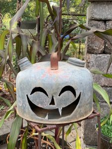 This faux pumpkin is a hollow jack-o-lantern face carved into a vintage, metal, dome gas can.