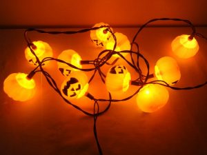 A lit vintage Halloween string of orange jack-o-lantern light bulbs.
