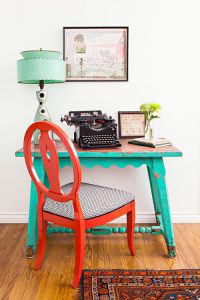 A turquoise desk with a vintage lamp, type writer, and red chair filling the rest of the scene.