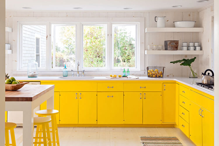 A kitchen housing bright yellow cabinets and stools contrasting with the rest of the white interior.