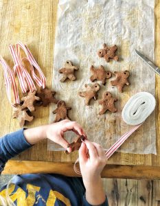 Child stringing together gingerbread tags onto a candy-striped ribbon.