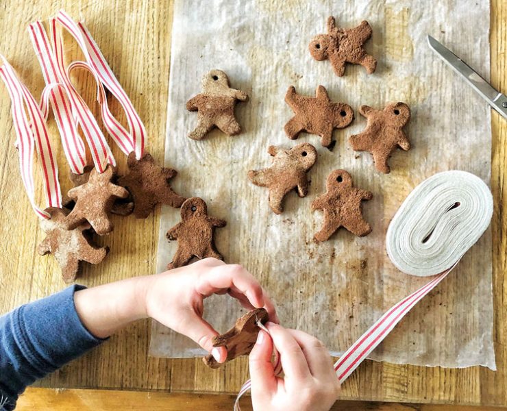 Child stringing together gingerbread tags onto a candy-striped ribbon.