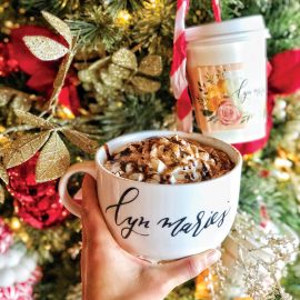 Hand holding coffee cup in front of a Christmas tree.