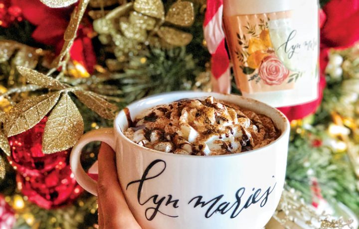 Hand holding coffee cup in front of a Christmas tree.