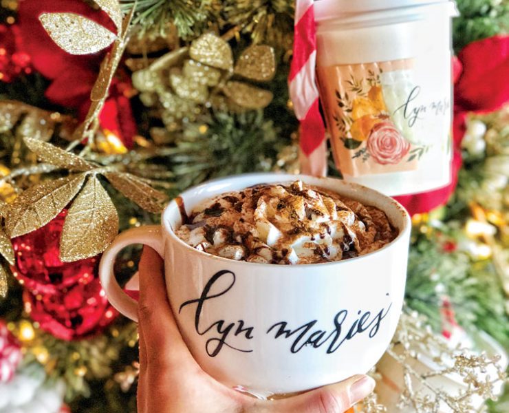 Hand holding coffee cup in front of a Christmas tree.