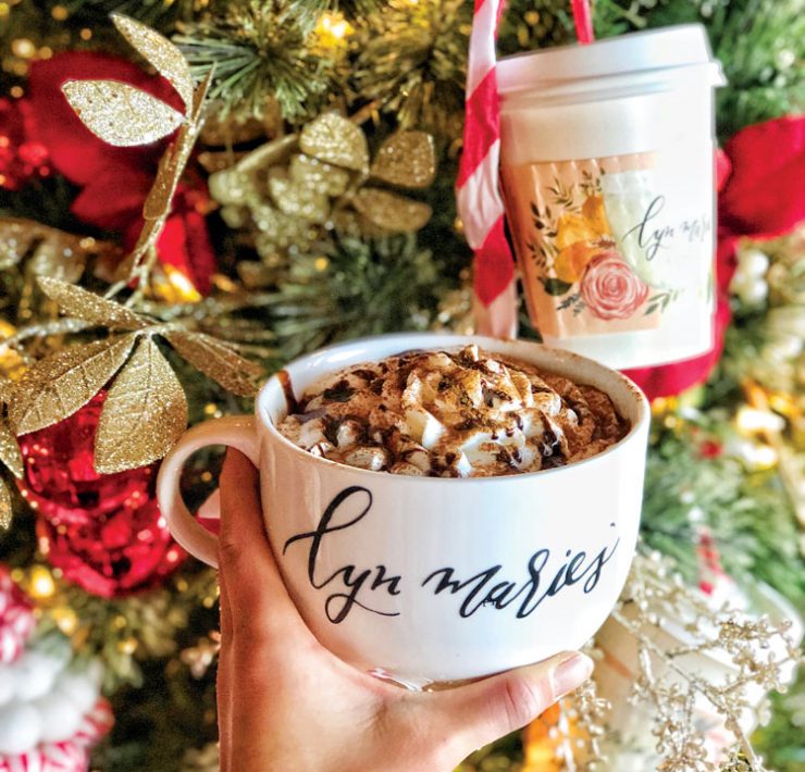 Hand holding coffee cup in front of a Christmas tree.