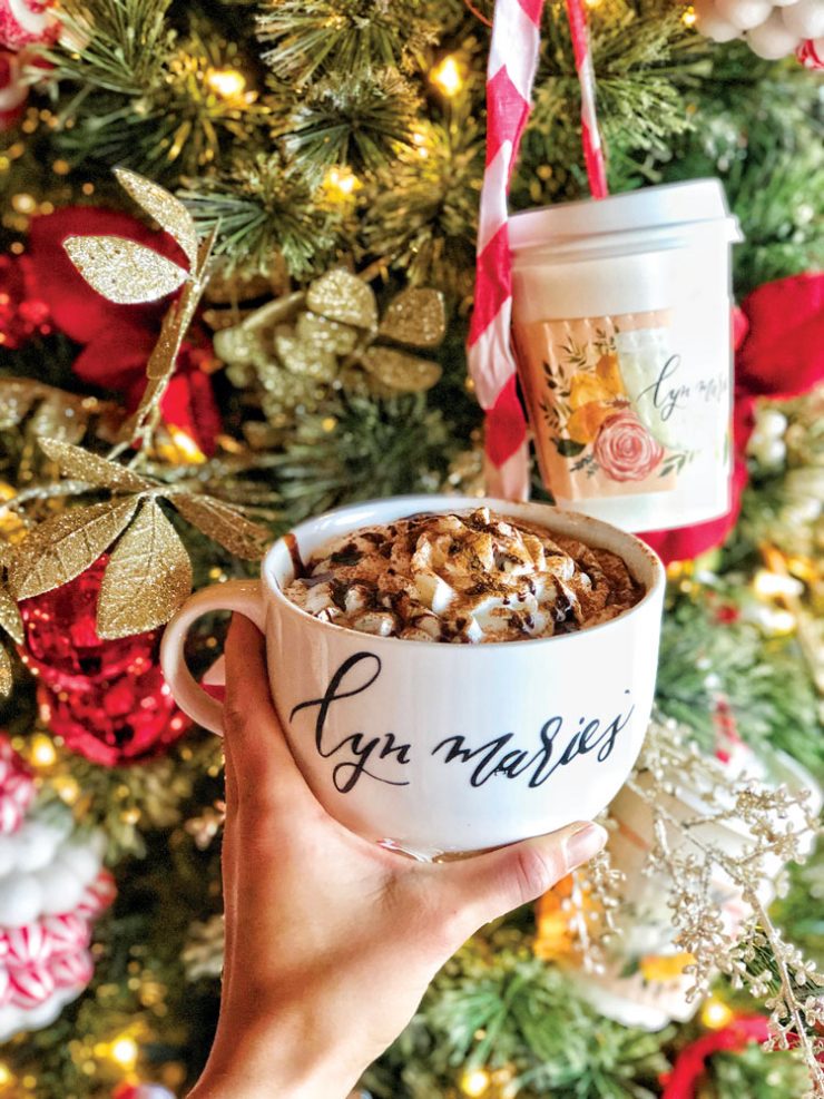 Hand holding coffee cup in front of a Christmas tree.