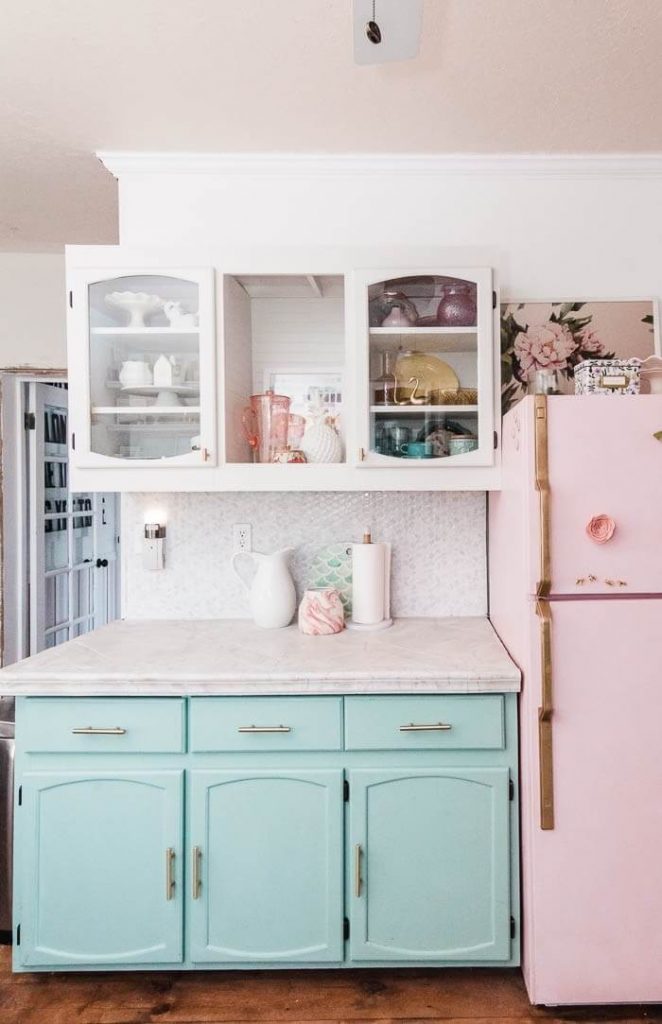 A kitchen composed of mint cabinets that complement the bubblegum pink countertop and fridge.
