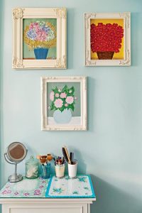 Gallery wall display with floral paintings over a makeup station vanity