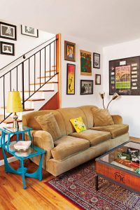 An English roll arm sofa upholstered in camel colored velvet with a music themed gallery wall display