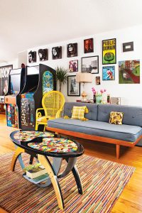 Music themed gallery wall above a mid century modern sofa and two vintage arcade games