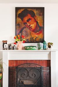 Fireplace with red brick surround, vintage cameras on the mantel and an Elvis Presley portrait hung on the wall above