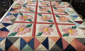 This quilt has a border made of triangles framing a square pattern. Each square has a large pick flower in the center,