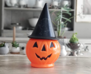 A vintage Halloween plastic jack-o-lantern wearing a black witch hat.