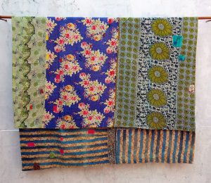 This quilt has a more prominent texture and has large strips of different patterns, including a bright blue floral and several olive-green patterns.