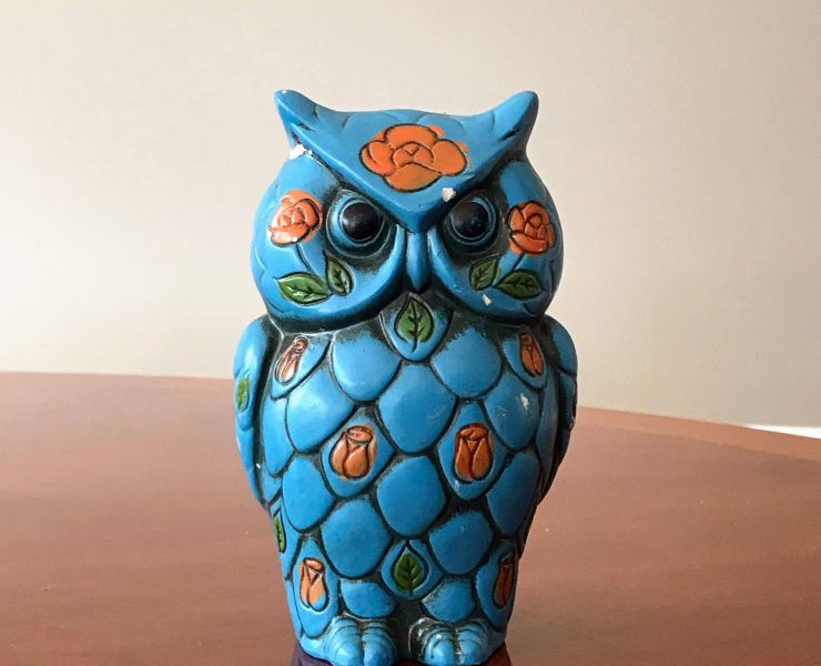 A teal ceramic owl coin bank with leafy orange flowers painted on it.