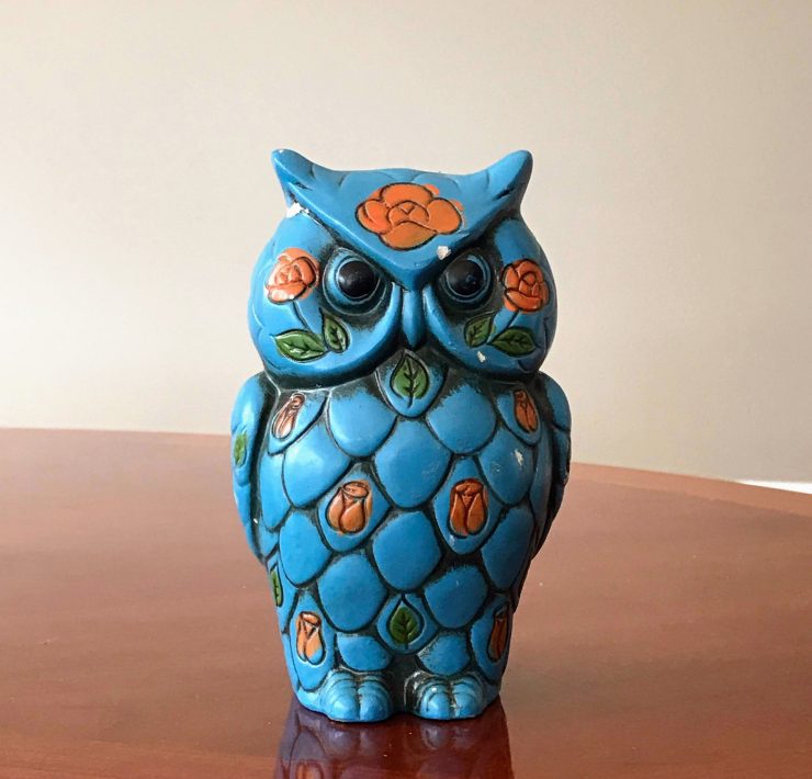A teal ceramic owl coin bank with leafy orange flowers painted on it.