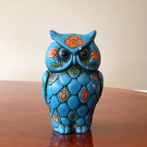 A teal ceramic owl coin bank with leafy orange flowers painted on it.