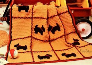 This mustard-colored knit blanket has squares framed by red stitched yarn with black Scottie dogs.