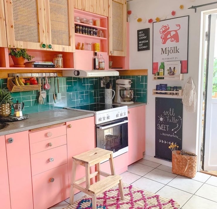 A kitchen with cabinets painted a soft pink, surrounded by a variety of eclectic decor