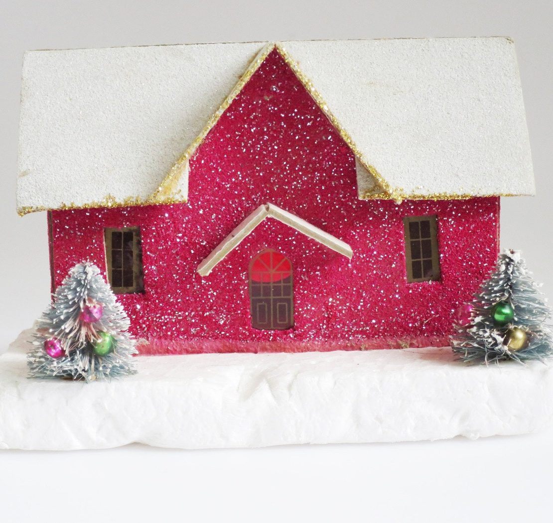 Glittery, magenta putz house with snow covered roof and two mini decorated trees in front of it.