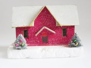 Glittery, magenta putz house with snow covered roof and two mini decorated trees in front of it.