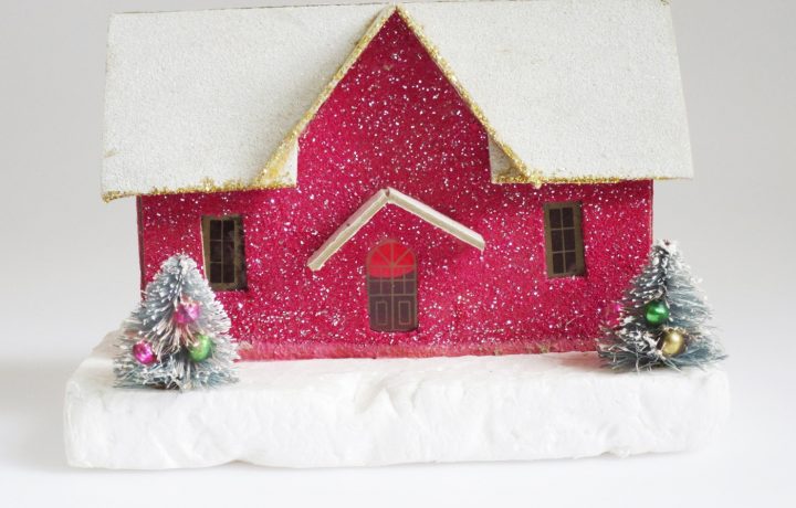 Glittery, magenta putz house with snow covered roof and two mini decorated trees in front of it.