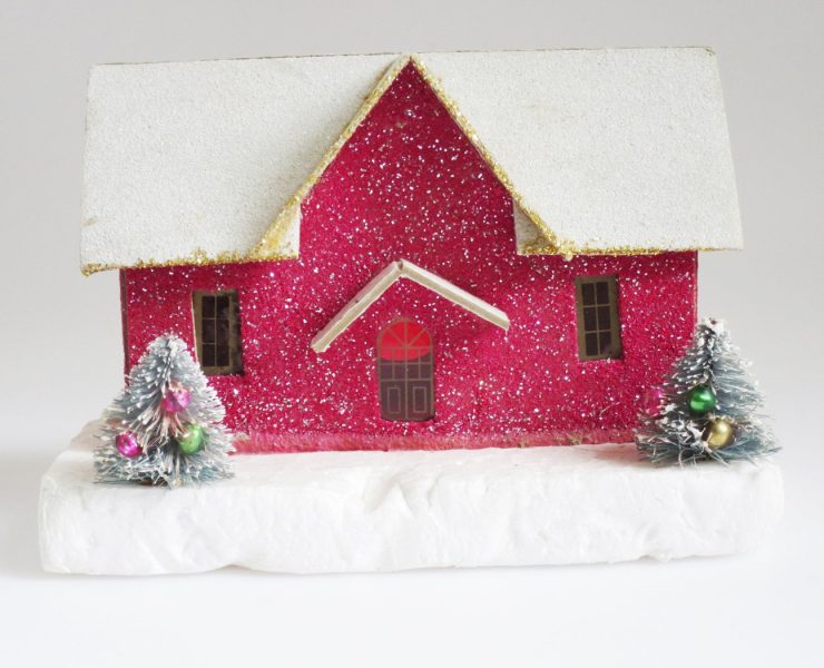 Glittery, magenta putz house with snow covered roof and two mini decorated trees in front of it.