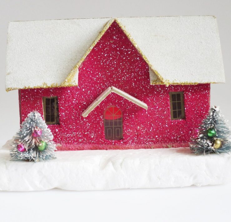 Glittery, magenta putz house with snow covered roof and two mini decorated trees in front of it.