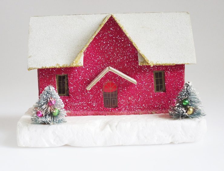 Glittery, magenta putz house with snow covered roof and two mini decorated trees in front of it.