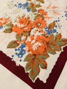 Vintage Thanksgiving tablecloth with maroon border, orange roses and small blue flowers.