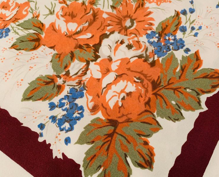 Vintage Thanksgiving tablecloth with maroon border, orange roses and small blue flowers.