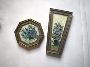 Two paintings in untraditionally shaped frames with thickly painted dusty-blue flowers in each.