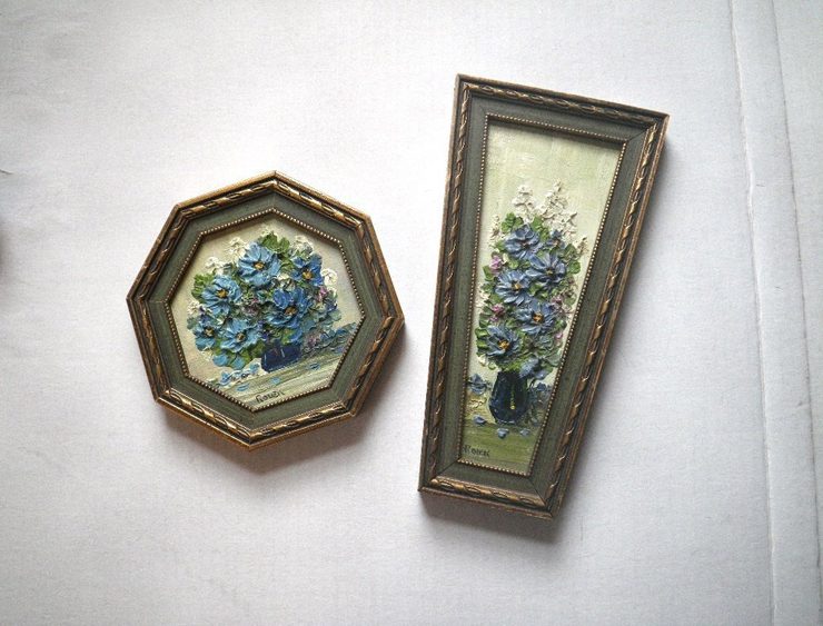 Two paintings in untraditionally shaped frames with thickly painted dusty-blue flowers in each.