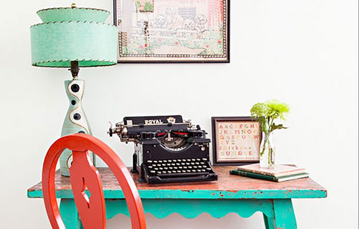 A turquoise desk with a vintage lamp, type writer, and red chair filling the rest of the scene.