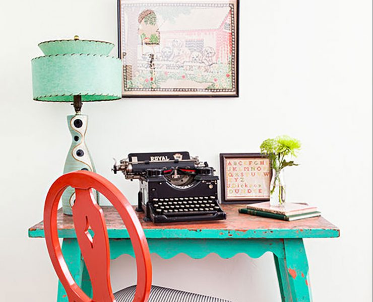 A turquoise desk with a vintage lamp, type writer, and red chair filling the rest of the scene.
