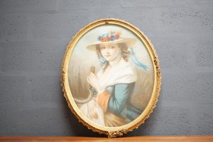 This vintage portrait shows a young girl in a middle-class, French dress holding a scythe and bail of wheat.